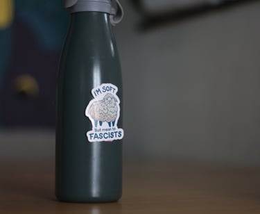 Dark green reusable water bottle with a sheep sticker saying I'm soft but mean to fascists.