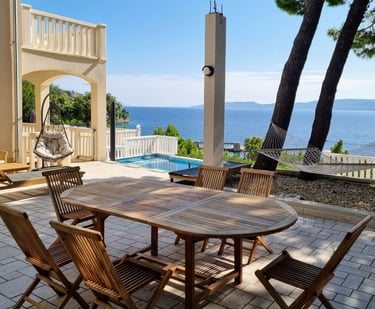 The photo shows a dining table, deck chairs and swings in the central courtyard overlooking the pool and the open sea.