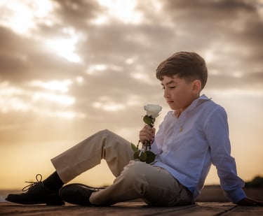 a boy sitting on a wooden deck with a flower