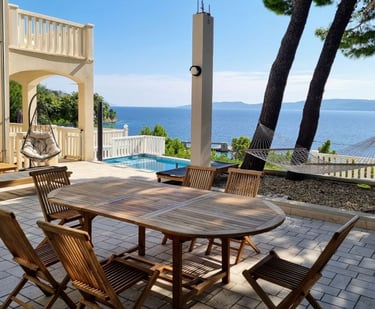 The photo shows a dining table, deck chairs and swings in the central courtyard overlooking the pool and the open sea.