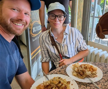 Moose and Bugs sitting at a cafe table enjoying traditional Balkan burek pastry on white plates.