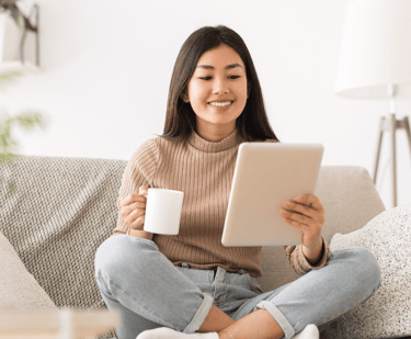a woman sitting on a couch holding a cup of coffee and a tablet