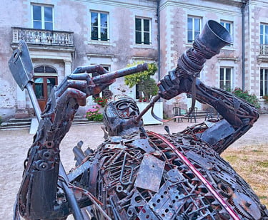 Intricate scrap metal sculpture of Capitaine Boyton outside a historic stone building in France.