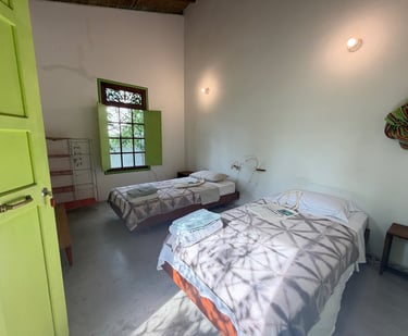 Rustic twin bedroom with green shutters, white walls, and cozy beds in a boutique guest house.