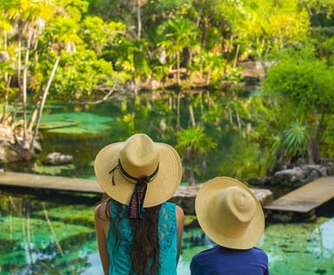 Dos viajeros con sombreros de paja contemplando un cenote de agua turquesa cristalina 