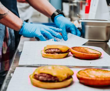 Montaje de hamburguesas en cocina de Flipa con pan tostado y guantes de preparación