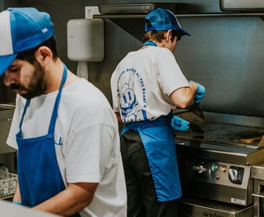 Cocineros de Flipa trabajando en cocina con uniforme azul y plancha caliente