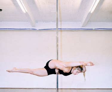 Vrouw in zwarte top doet een paaldans oefening met paaldanspaal bij De Polecats Fabriek in Gent