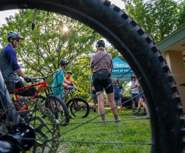Photo of people standing with their bikes in the background of a close up shot of a bike tire