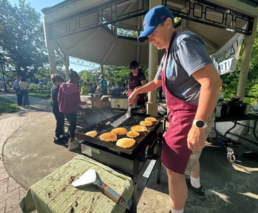 Kids in the background of a person flipping pancakes on a griddle in a park