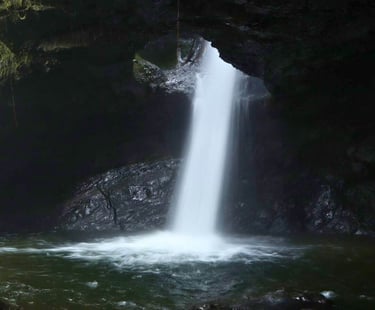 A scenic underground waterfall cascading through a dark rocky cave into a natural pool.