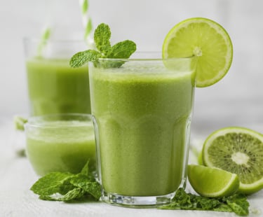 A glass of green smoothie garnished with mint and lime.