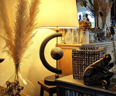 Modern black table lamp with warm lighting on a wooden stand surrounded by boho home decor and dried pampas grass.
