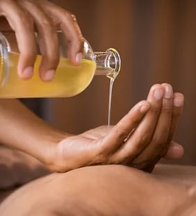 Une personne tient une bouteille d'huile d'un main. Elle verse un filet d'huile dans son autre main.