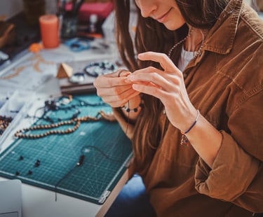 Artesana creando collares hechos a mano con cuentas y herramientas de joyería sobre mesa de trabajo.