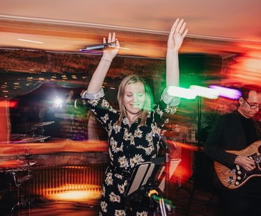 a woman in a floral jumpsuit dancing with a guitar at wedding party