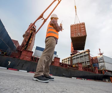 A port worker oversees a crane lifting a shipping container at a busy logistics terminal.