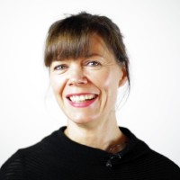 Professional headshot of a smiling Dr Fiona Flynn with brown hair and bangs wearing a black top.