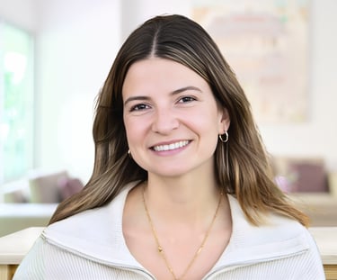 Professional headshot of a smiling young woman with brown hair wearing a white zip-up sweater.
