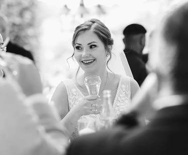 Photo en noir et blanc d'une mariée qui sourit, une coupe de champagne à la main.
