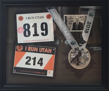 Shadow box display with I Run Utah marathon bibs, a 2018 finisher medal, and a commemorative photo.