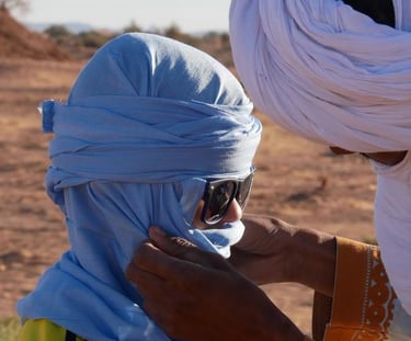 A nomad guide helps a boy arrange his cheche or head covering 
