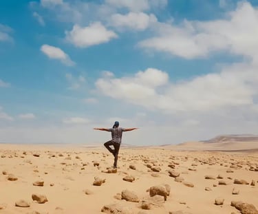 A woman stands on one leg doing a yoga move in the desert