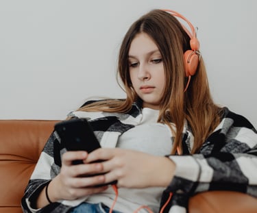 Teenage girl relaxing on a couch looking at her phone, appearing thoughtful and low-energy.