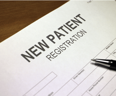 A black pen resting on a medical new patient registration form on a wooden desk.
