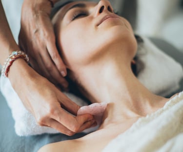 Professional aesthetician performs a facial gua sha massage using a rose quartz stone on a woman's neck.