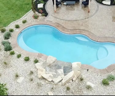 Freeform pool with attached spa, deep teal water and warm beige mosaic tile interior.