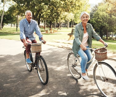 White haired woman and man ride bicycles next to park after treatment with acupuncture for pain