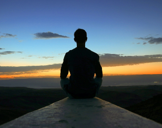 A person sitting looking at the sunset meditating