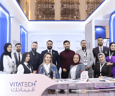 Professional Vitatech team posing at SAAM EVENT booth with blue LED lighting.