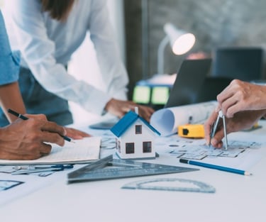 Architects working on blue prints and a house model for home design planning.