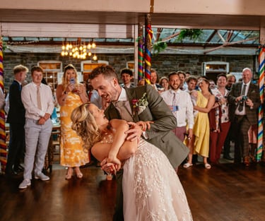 First dance dip at Plas Dinam Country House, the couple beaming as guests cheer them on in the vibrant reception hall.