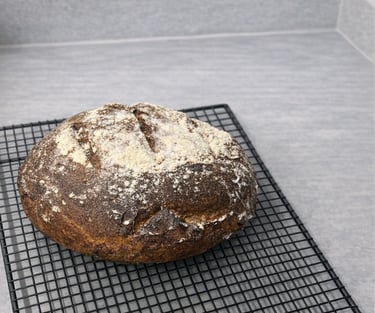 Freshly baked gluten-free artisan bread cooling on a black wire rack atop a grey countertop.