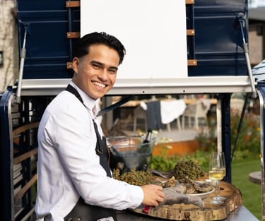 Vrolijk lachende medewerker opent oesters voor de Xagis tuc-tuc foodtruck.