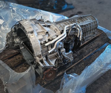 Audi A6 automatic car transmission unit sitting on a wooden pallet in an auto repair shop.