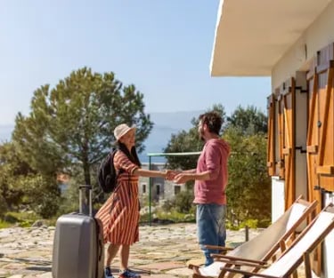 A woman with luggage checking into a sunny Mediterranean villa rental for a summer vacation.