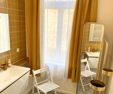 Salle de bain élégante avec carrelage jaune, lavabo moderne et grande fenêtre.