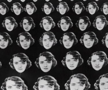 Chorus girls holding multiple large cardboard cutouts of Ruby Keeler’s face against a dark backgroun
