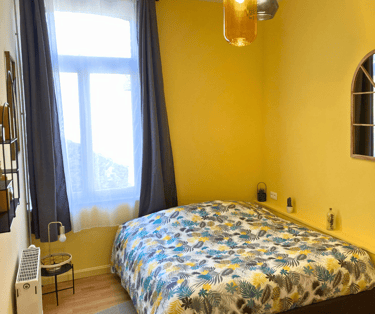 Chambre lumineuse avec lit double et mur jaune dans maison meublée.