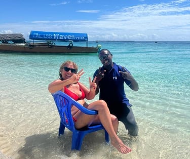 Smiling tourist sitting on a chair at Nakupenda Beach, Zanzibar, accompanied by a friendly local tour guide by the clear wate