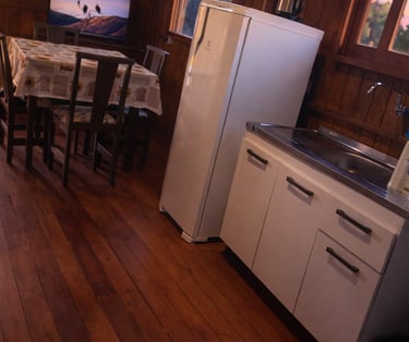 parte interna da cabana, a cozinha, com geladeira, pia, armários, mesa e TV 