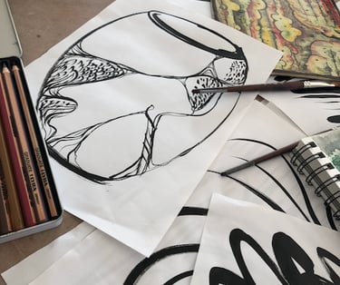 A display of black ink drawings with a vase sketch on top, pencils and notebook