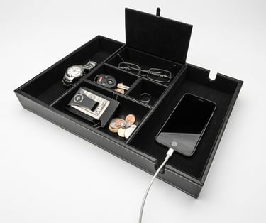 Black leather valet tray organizer for men holding a watch, wallet, coins, and charging smartphone.