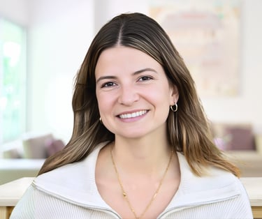 Professional headshot of a smiling young woman with brown hair wearing a white zip-up sweater.
