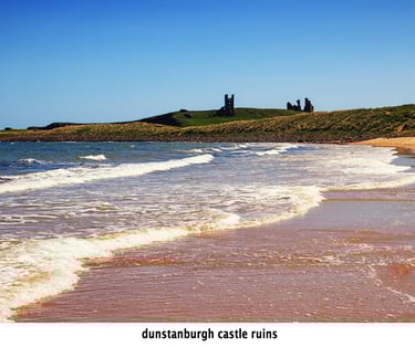 looking along a pattern of waves on the beach with dunstanburgh castle ruins in the background