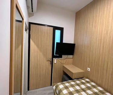 Kamar premium Kos Si Bos dengan meja kerja, kursi, lemari besar, dan Smart TV terpasang di dinding.